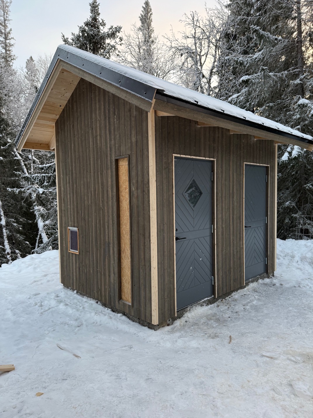 Nybyggt mörkt förråd i vintermiljö med dubbeldörr